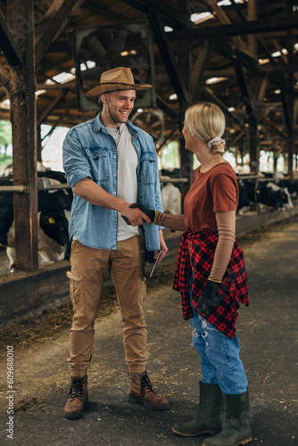 A man with a leghorn shakes hands with a woman working in a stable.