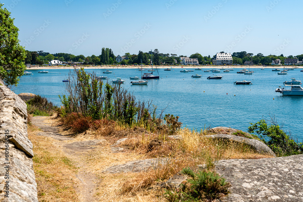 Summer stroll in Concarneau Bay, Brittany, France. The blue of the sky gives a beautiful emerald hue to the ocean. A few boats in and out of the bay.
