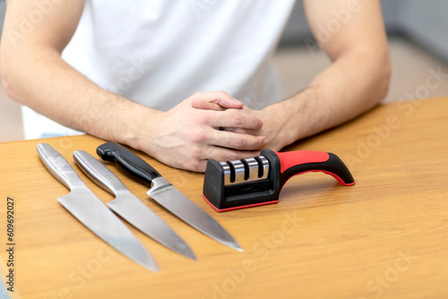 Close-up photo of man sharpening knives with special knife sharpener at home 