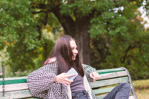 A relaxed young woman is sitting on a park bench with a satisfied expression on her face.