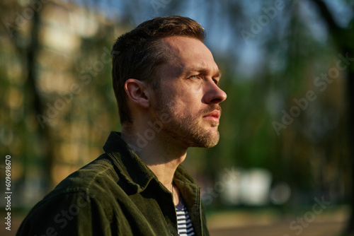 Young man smiling confident standing at park in the sunlight looking aside thoughtfully . High quality photo