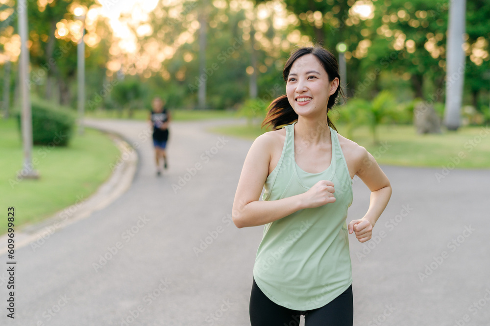 Fit Asian young woman jogging in park smiling happy running and enjoying a healthy outdoor lifestyle. Female jogger. Fitness runner girl in public park. healthy lifestyle and wellness being concept Fit Asian young woman jogging in park smiling happy running and enjoying a healthy outdoor lifestyle. Female jogger. Fitness runner girl in public park. healthy lifestyle and wellness being concept