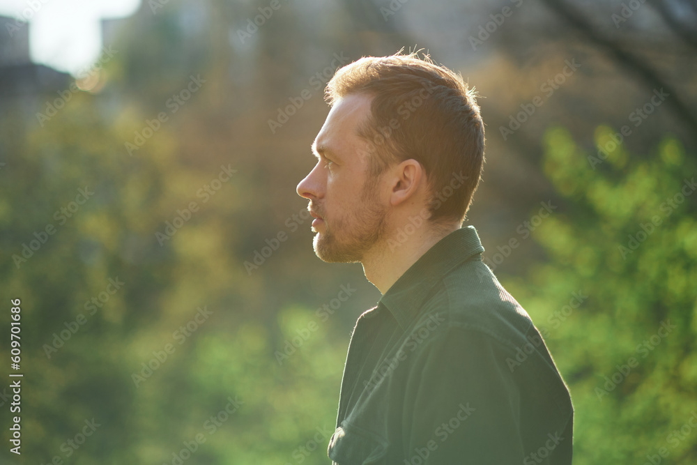 Young man smiling confident standing at park in the sunlight looking aside thoughtfully . High quality photo Young man smiling confident standing at park in the sunlight looking aside thoughtfully . High quality photo