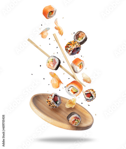 Various fresh sushi rolls with ginger falling on a wooden plate