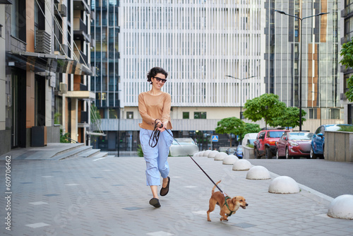 Young pretty female adult with small ginger dog in the bi city walking having fun. City view High quality photo