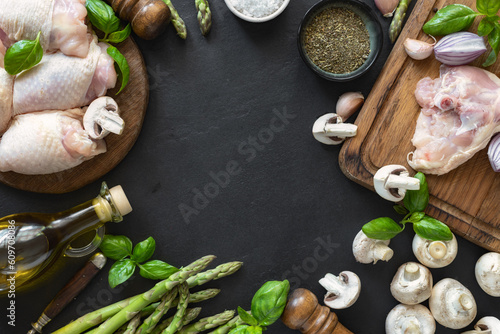 Frame of fresh pieces of chicken thigh meat on wooden cutting board with ingredients for cooking healthy food on dark background top view