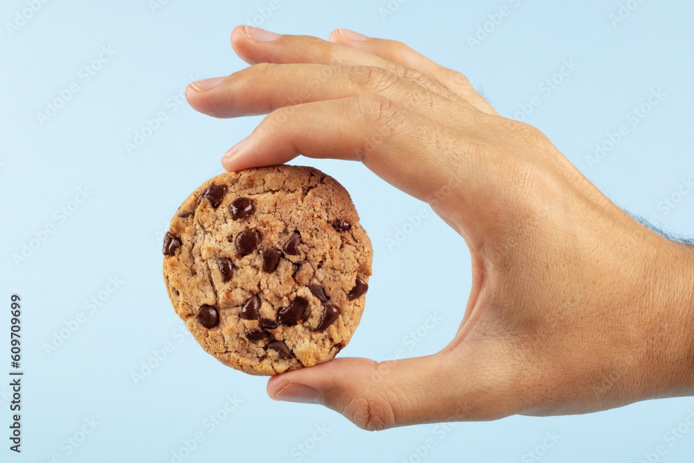 Man's hand holding a chocolate chip cookie on a blue background. Man's hand holding a chocolate chip cookie on a blue background.