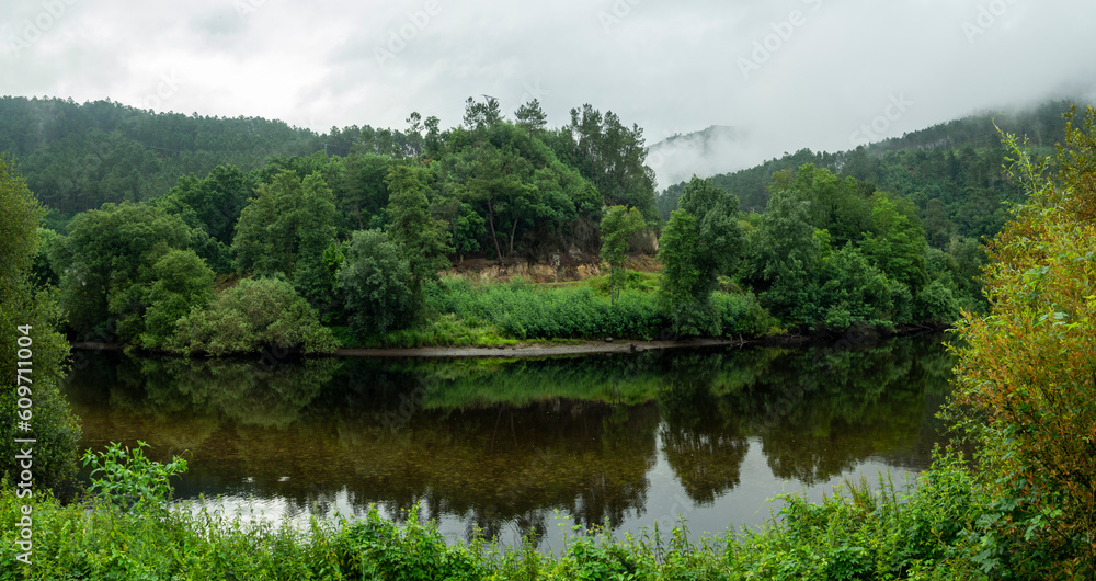 Obraz premium View of the green fluvial landscape reflected in the waters of the Confluence of the Miño river and the Avia river, Ribadavia Orense, summer of 2021, Spain