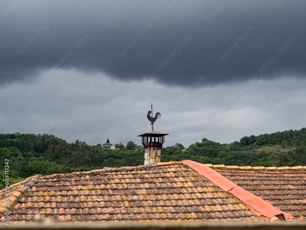 Dark storm cloud, with a rooster-shaped weather vane on an ocher roof. Dark storm cloud, with a rooster-shaped weather vane on an ocher roof.