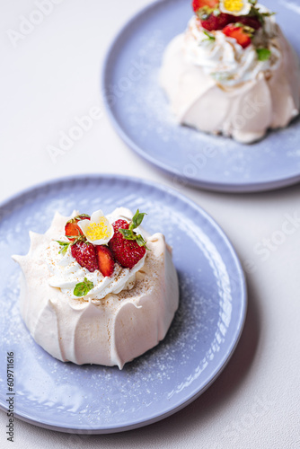 Two small pavlova cakes from meringue decorated with fresh strawberries on a pink plate. Bright scene with flowers as decoration.