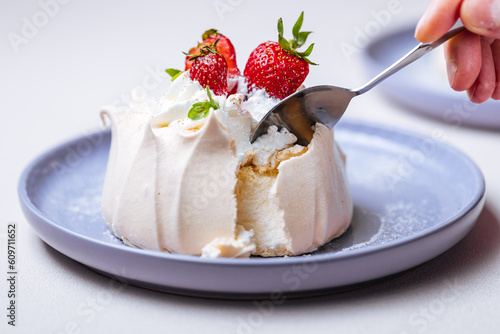 Two small pavlova cakes from meringue decorated with fresh strawberries on a pink plate. Bright scene with flowers as decoration.