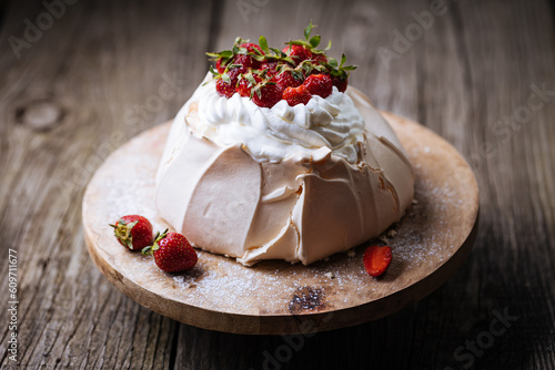 Pavlova cake decorated with strawberries in rustic, wooden atmosphere. Cake is made from meringue and whipped cream