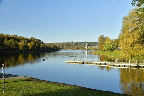 Le lac des Doyards et le village de Vielsalm avec l'église paroissiale Saint Gengoux se reflétant dans ses eaux  sous un ciel clair d'automne  photo