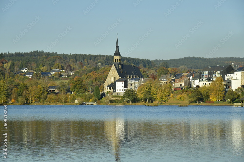 Le lac des Doyards et le village de Vielsalm avec l'église paroissiale Saint Gengoux se reflétant dans ses eaux  sous un ciel clair d'automne 