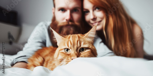 Happy smiling couple sitting on bed with their ginger cat, enjoying relaxed morning at home 