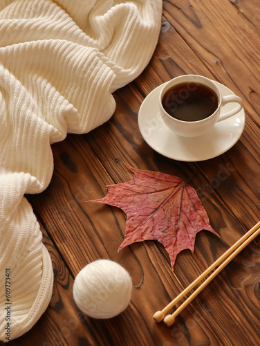 Knitting needles, ball of wool, cup of coffee and autumn leave on wooden background