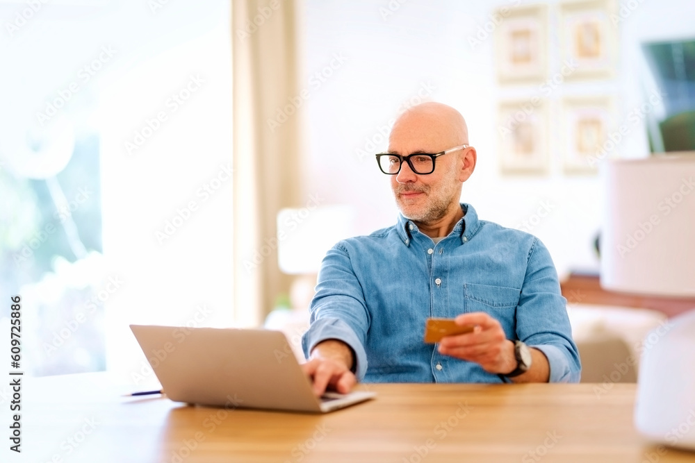 Man sitting in living room with laptop and using credit card Man sitting in living room with laptop and using credit card