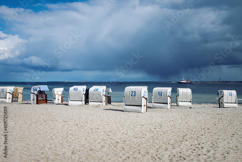 Sandy beach on the coast of the Baltic Sea in Strande / Kiel in Germany. With several beach chairs, a ferry and dark clouds after a rain shower.