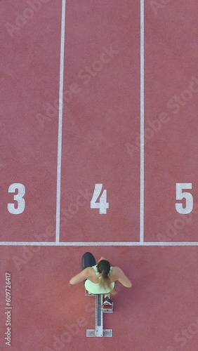 Vertical video of caucasian female athlete alone on the athletic track, sprint running in line four, aerial directly above view. photo