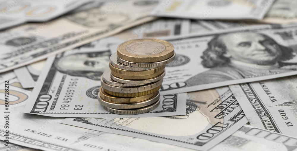 Stack of golden coins on dollar bills on a table.
