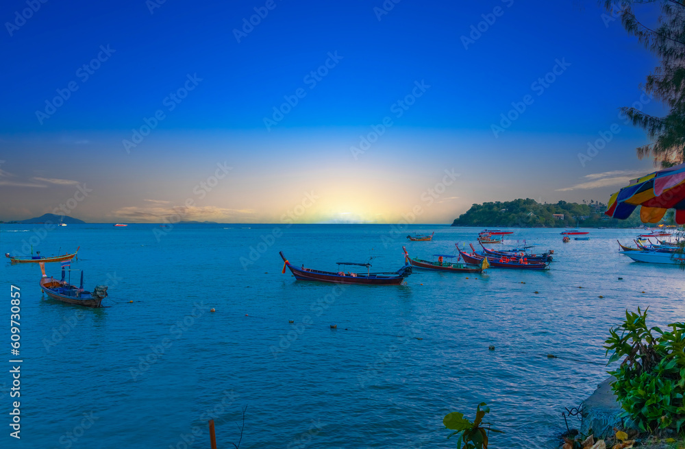 Colourful Skies Sunset over Rawai Beach in Phuket island Thailand. Lovely turquoise blue waters, lush green mountains colourful skies and beautiful views the pier and longtail boats and islands 