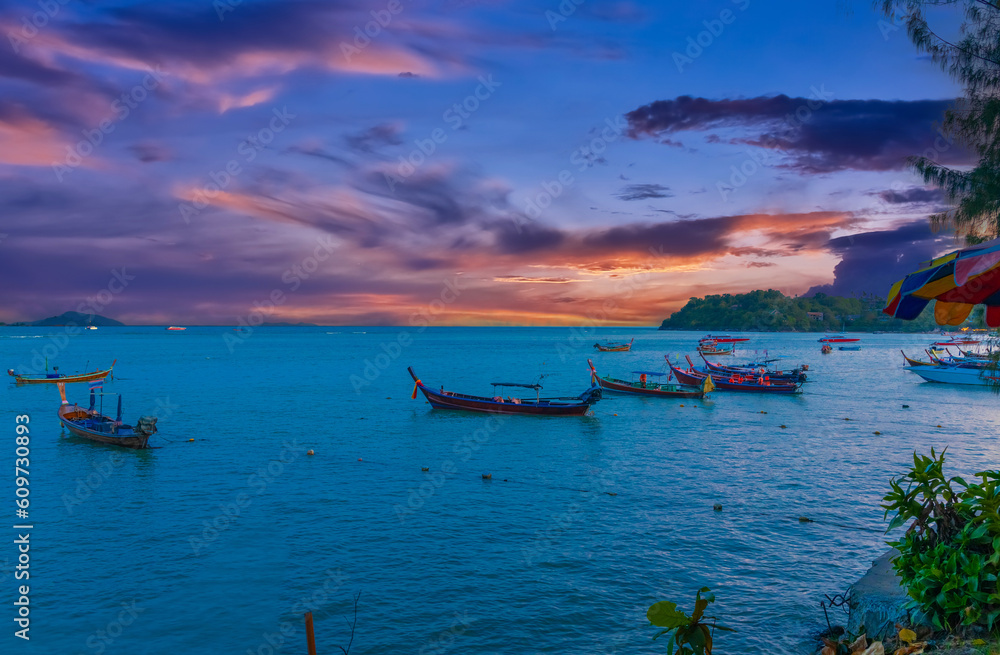Colourful Skies Sunset over Rawai Beach in Phuket island Thailand. Lovely turquoise blue waters, lush green mountains colourful skies and beautiful views the pier and longtail boats and islands Colourful Skies Sunset over Rawai Beach in Phuket island Thailand. Lovely turquoise blue waters, lush green mountains colourful skies and beautiful views the pier and longtail boats and islands