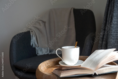 Armchair warm blanket opened book with teacup on wooden table