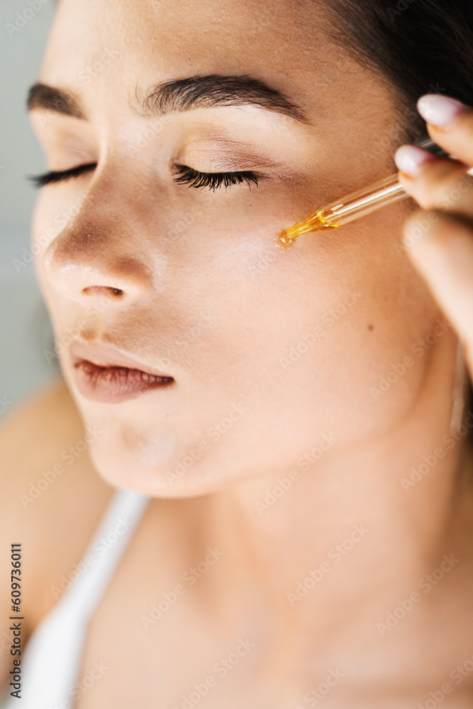 Attractive girl drops essential oil on facial skin close-up. Young woman is applying moisturizing serum on her face.