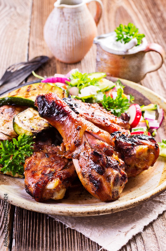 Traditional barbecue chicken drumsticks with grilled vegetable and lettuce served as close-up on a rustic design plate