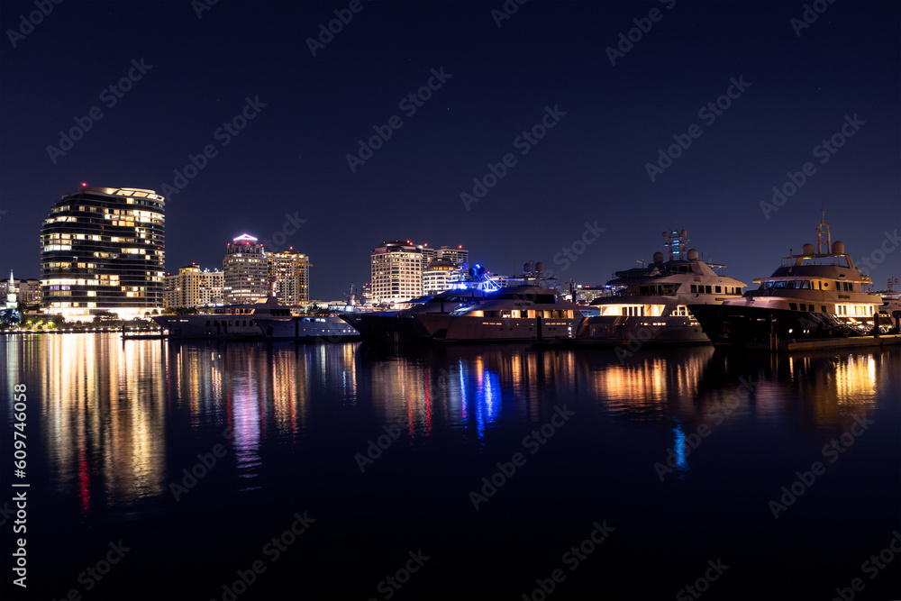 Yachts docked in a marina at night in Palm Beach with the downtown West Palm Beach skyline in the background