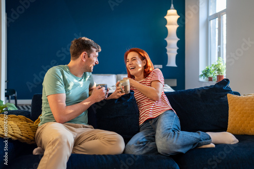Картината върху платно Happy couple in love joking laughing while relaxing on couch with cup coffee, bonding, enjoying moment time together at home
