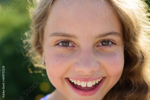 Cute little smiling happy girl close up face. Outdoor closeup portrait of funny kids face. Summer kid outdoor portrait. Close up face of cute child. Kid having fun outdoor on summer day.