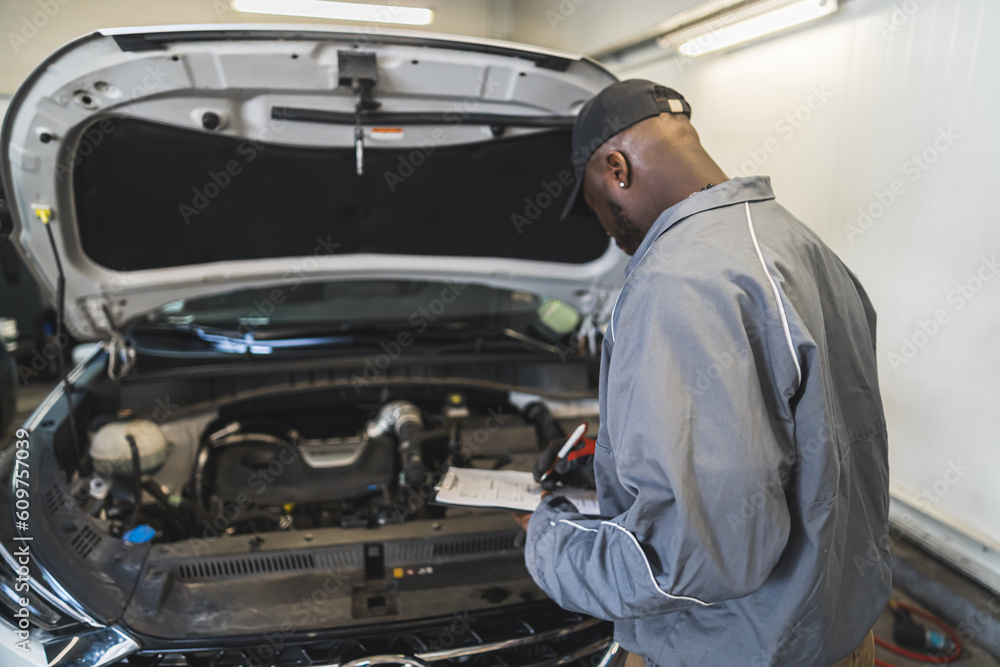 Mechanic checking car engine under the open hood at a service shop. High quality photo Mechanic checking car engine under the open hood at a service shop. High quality photo