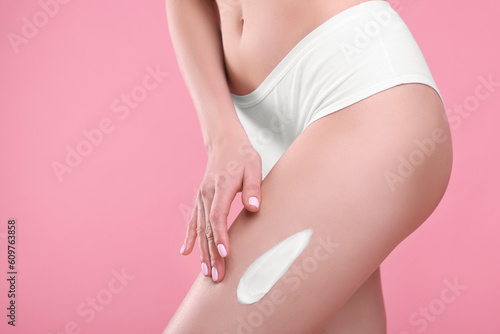 Woman with smear of body cream on her leg against pink background, closeup. Space for text