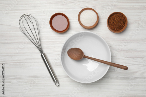 Flat lay composition with instant coffee granules and whisk on white wooden table