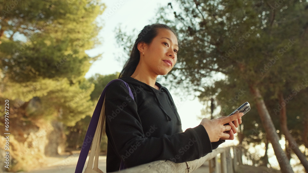 Fototapeta premium Young woman walks along the path and uses mobile phone