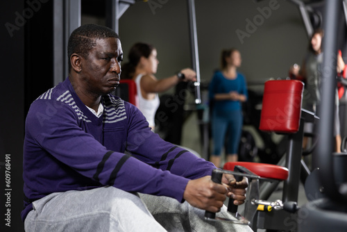 African american man is engaged in a simulator with horizontal weights in the gym