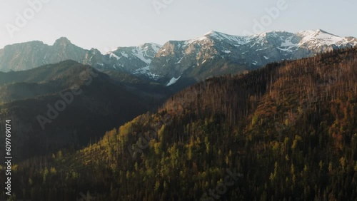 Stunning view high mountain peaks covered with snow lit with warm sunrise or sunset light, aerial drone shot of beautiful mountains and hills, spring season early morning, mountain range golden hour