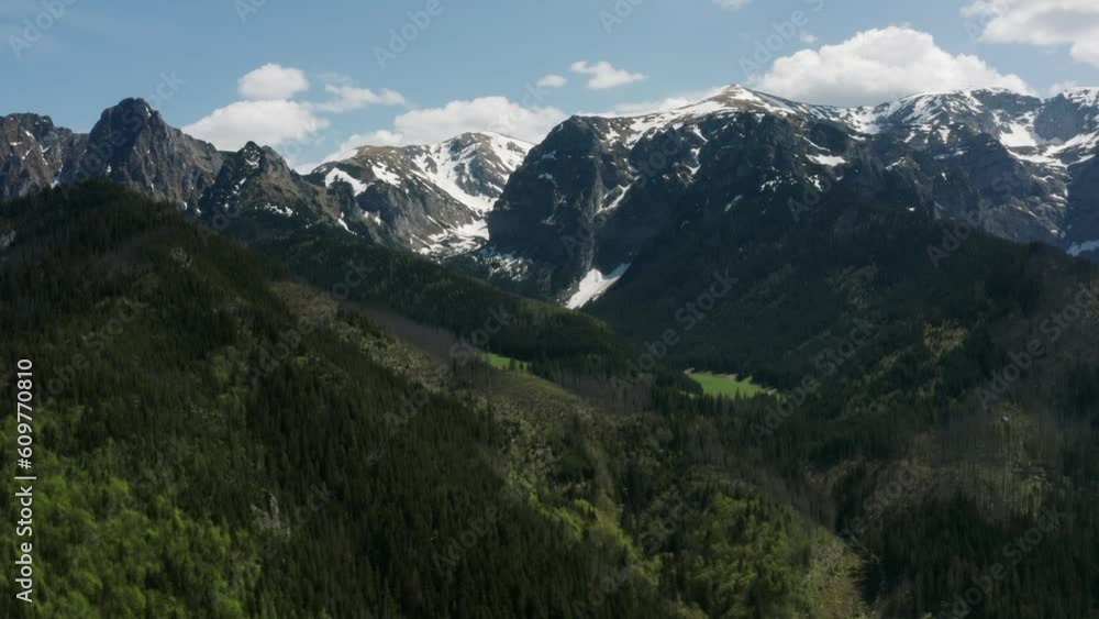 Top view mountain valley, high peaks covered with snow bright sun light, daylight, stunning aerial drone shot snowy mountains and green hills with pine trees, spring season mountain range landscape Top view mountain valley, high peaks covered with snow bright sun light, daylight, stunning aerial drone shot snowy mountains and green hills with pine trees, spring season mountain range landscape