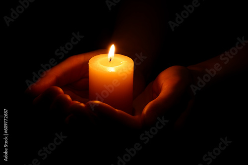 Woman holding burning candle in hands on black background, closeup