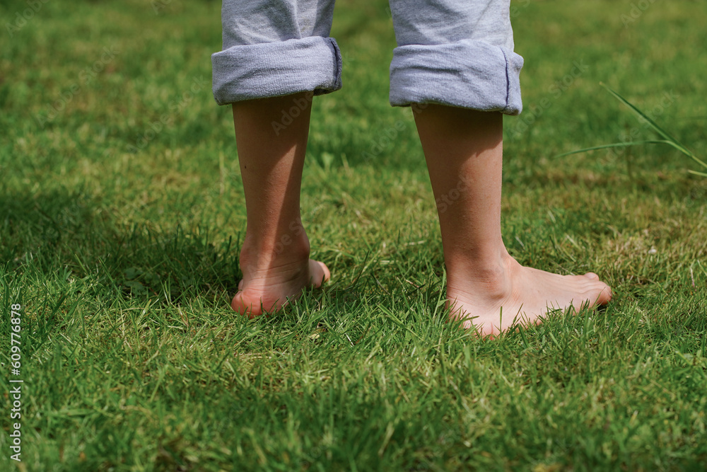 Happy child is barefoot on the grass, close-up feet. Sunny summer day. Summer Vacation in the village. Dangers of Tick-Borne Diseases, Lyme disease, encephalitis. World Soil Day