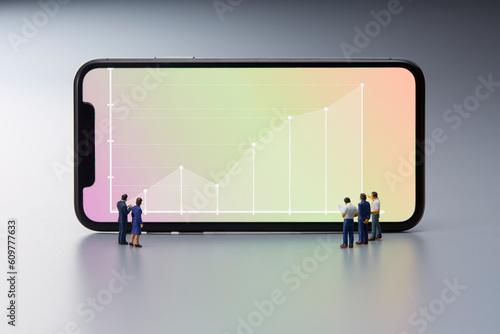 スマートフォンに表示されたグラフとミニチュア人形