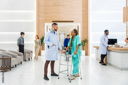 Caucasian doctors support patient walk through the hallway in hospital.