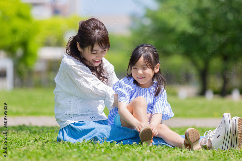 娘を膝に乗せて芝生に座る母親 娘を膝に乗せて芝生に座る母親
