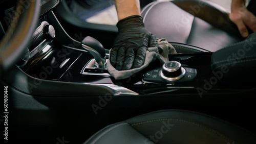 Detail of male car service worker performing dry cleaning and washing interior of a luxury car and gear selector with microfiber cloth