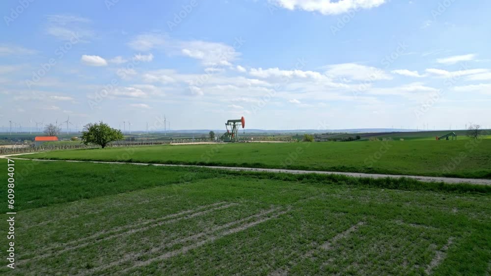 Drone Approach Towards Pump Jack Extracting Gas From Oil Field. Wind Farm In Distance. low aerial Drone Approach Towards Pump Jack Extracting Gas From Oil Field. Wind Farm In Distance. low aerial