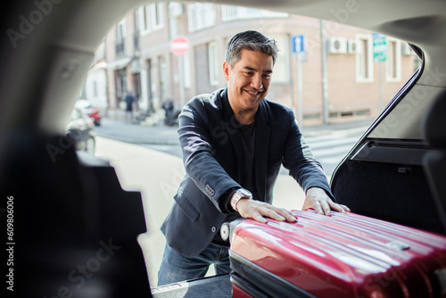Middle aged man putting a suitcase in the trunk of a car