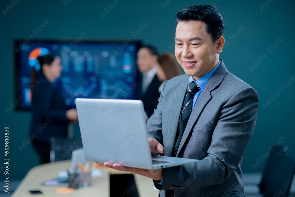 Handsome business man and suit holding the laptop in his hands and writing something. Side view, standing confident in the office in front of his team. Handsome business man and suit holding the laptop in his hands and writing something. Side view, standing confident in the office in front of his team.