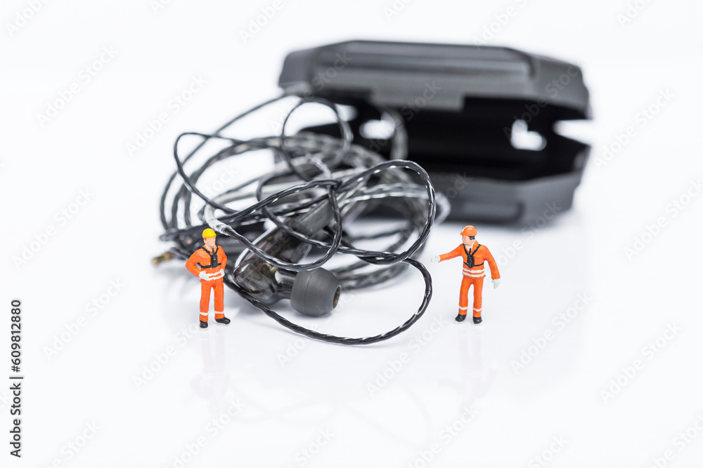 Tangled earphones cable with miniature worker isolate on white background, worker fixing messy wire Tangled earphones cable with miniature worker isolate on white background, worker fixing messy wire