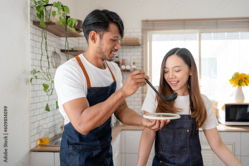 Asian couple happily prepare ingredient for breakfast in modern and stylish kitchen. Young Asian couple happily wearing apron and cooking together. Asian couple happily prepare ingredient for breakfast in modern and stylish kitchen. Young Asian couple happily wearing apron and cooking together.